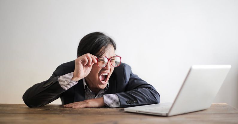 Entrepreneur Mistakes - Modern Asian man in jacket and glasses looking at laptop and screaming with mouth wide opened on white background